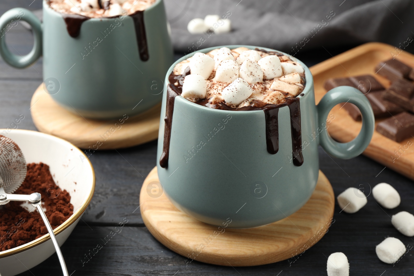 Photo of Cups of aromatic hot chocolate with marshmallows and cocoa powder on dark gray wooden table, closeup