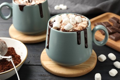 Cups of aromatic hot chocolate with marshmallows and cocoa powder on dark gray wooden table, closeup