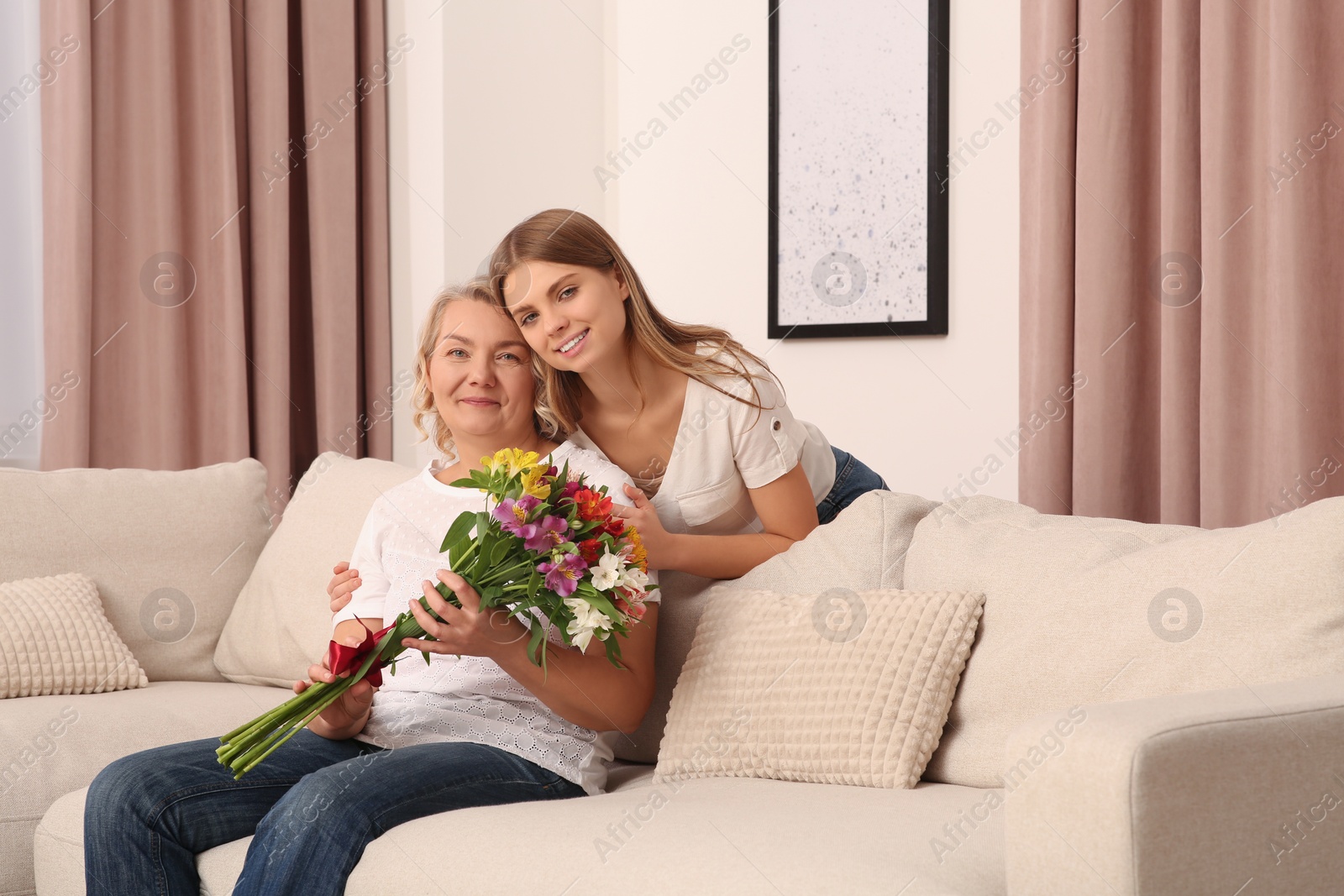 Photo of Young daughter congratulating her mom with flowers at home. Happy Mother's Day