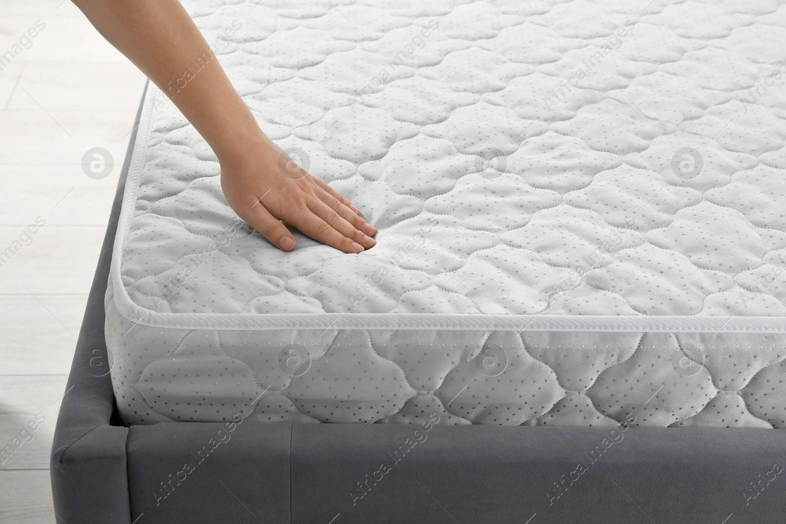 Photo of Woman touching soft light green mattress indoors, closeup