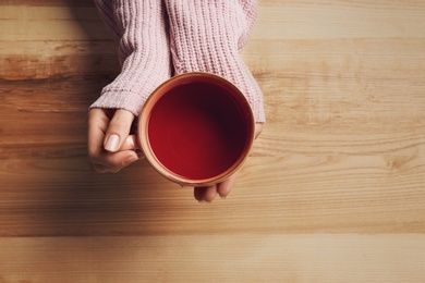 Photo of Woman holding cup of tea at wooden table, top view