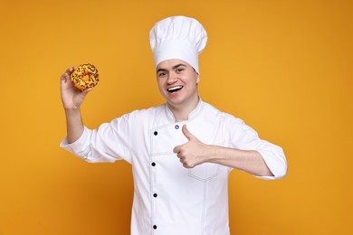 Portrait of happy confectioner in uniform holding donut on orange background