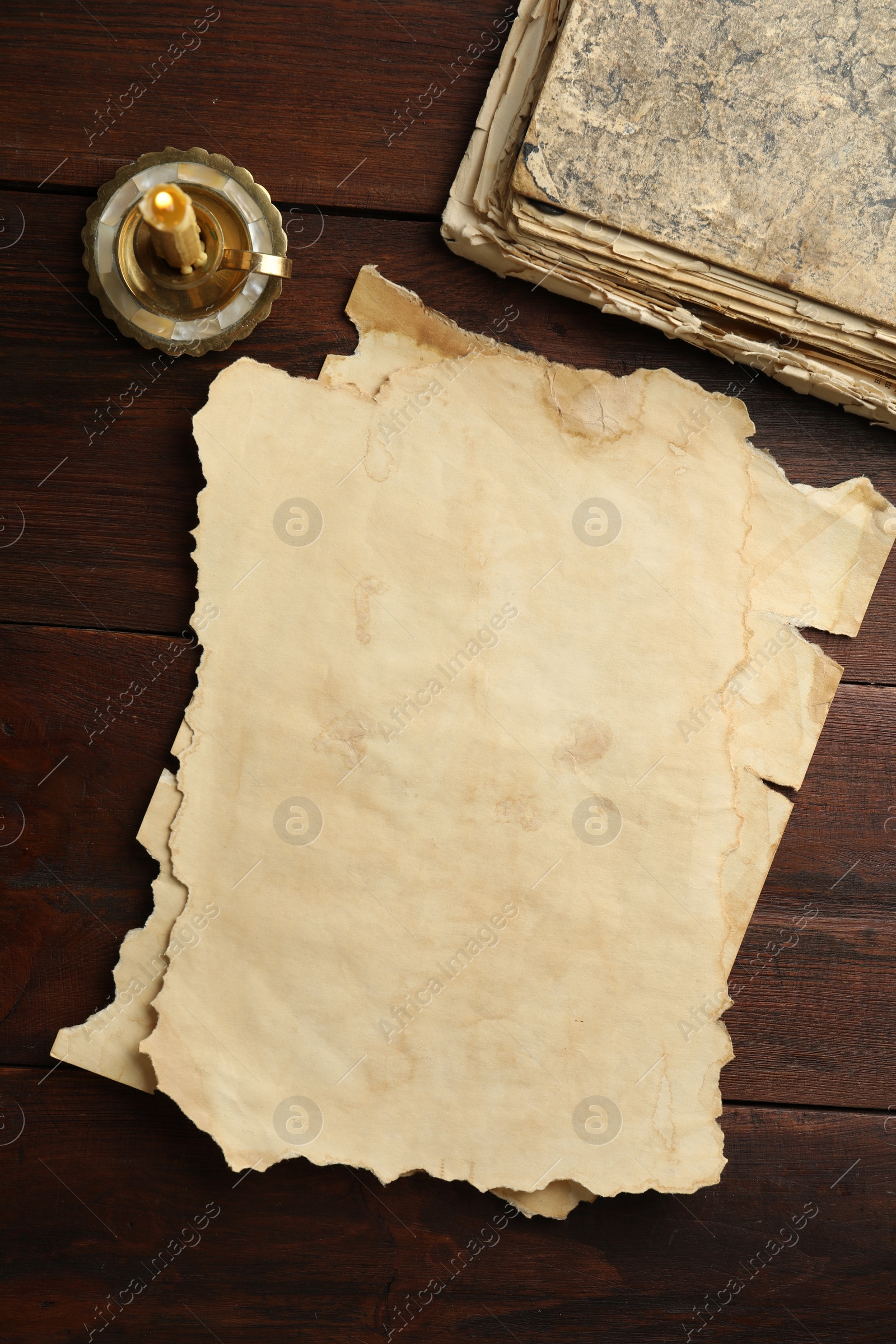 Photo of Sheets of old parchment paper, vintage book and candle on wooden table, flat lay