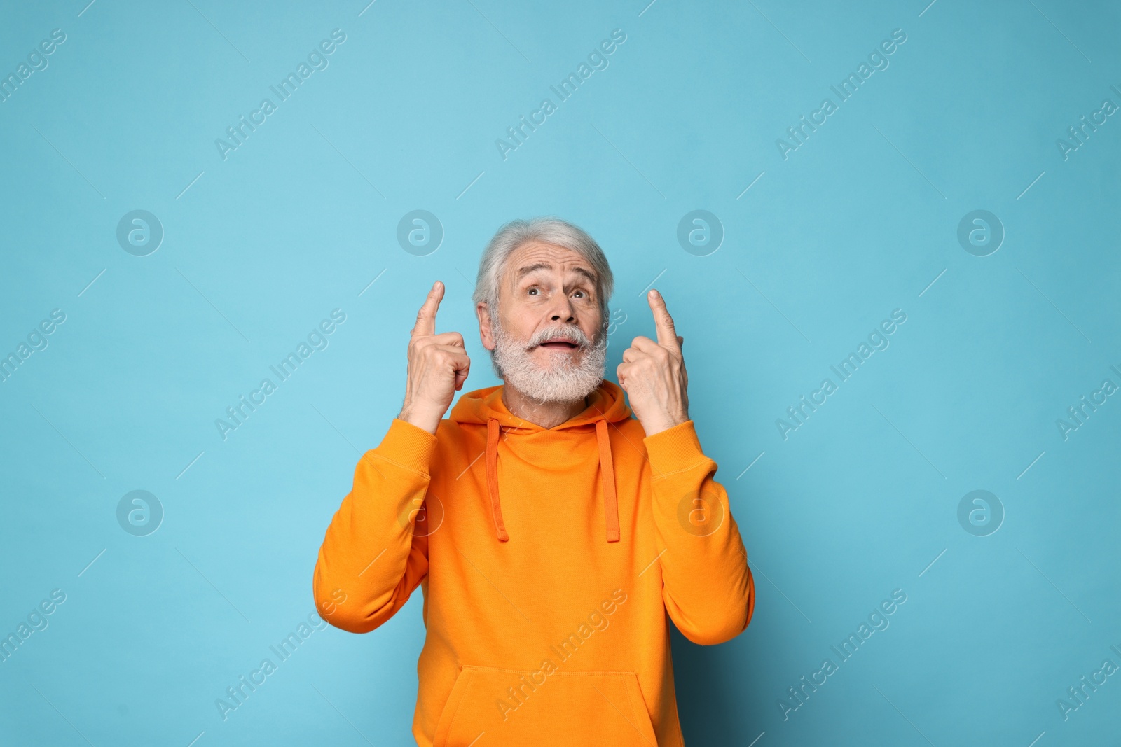 Photo of Senior man with mustache pointing at something on light blue background