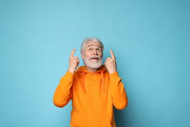 Senior man with mustache pointing at something on light blue background