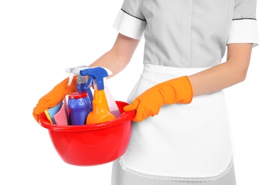 Young chambermaid holding basin with cleaning supplies on white background