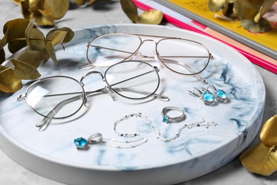 Glasses in stylish frames, leaves and jewelry on grey table