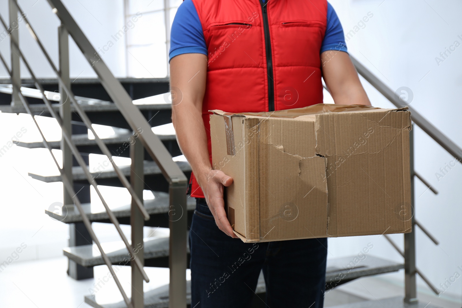 Photo of Courier with damaged cardboard box indoors, closeup. Poor quality delivery service