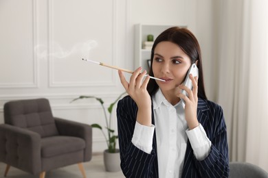 Photo of Woman using long cigarette holder for smoking and talking on phone in office