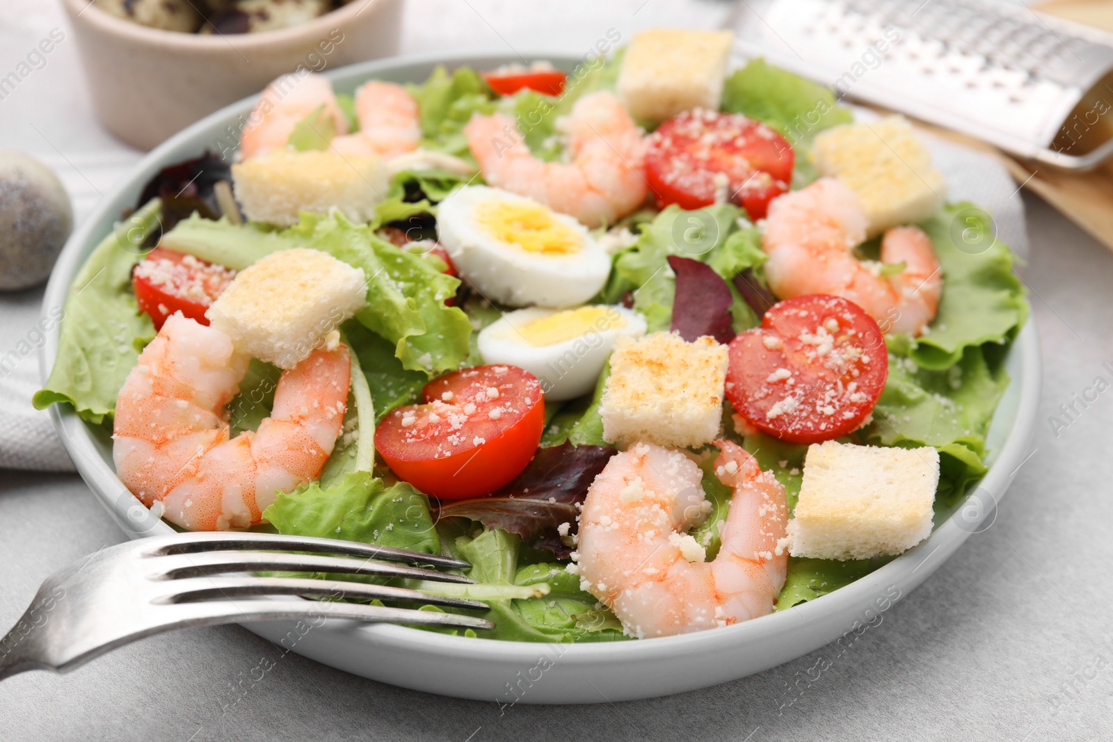 Photo of Delicious Caesar salad with shrimps and fork served on light table, closeup