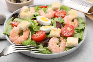 Delicious Caesar salad with shrimps and fork served on light table, closeup