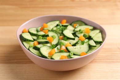 Photo of Tasty fresh salad with cucumber in bowl on wooden table, closeup