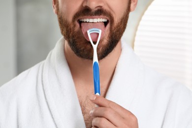 Man brushing his tongue with cleaner indoors, closeup