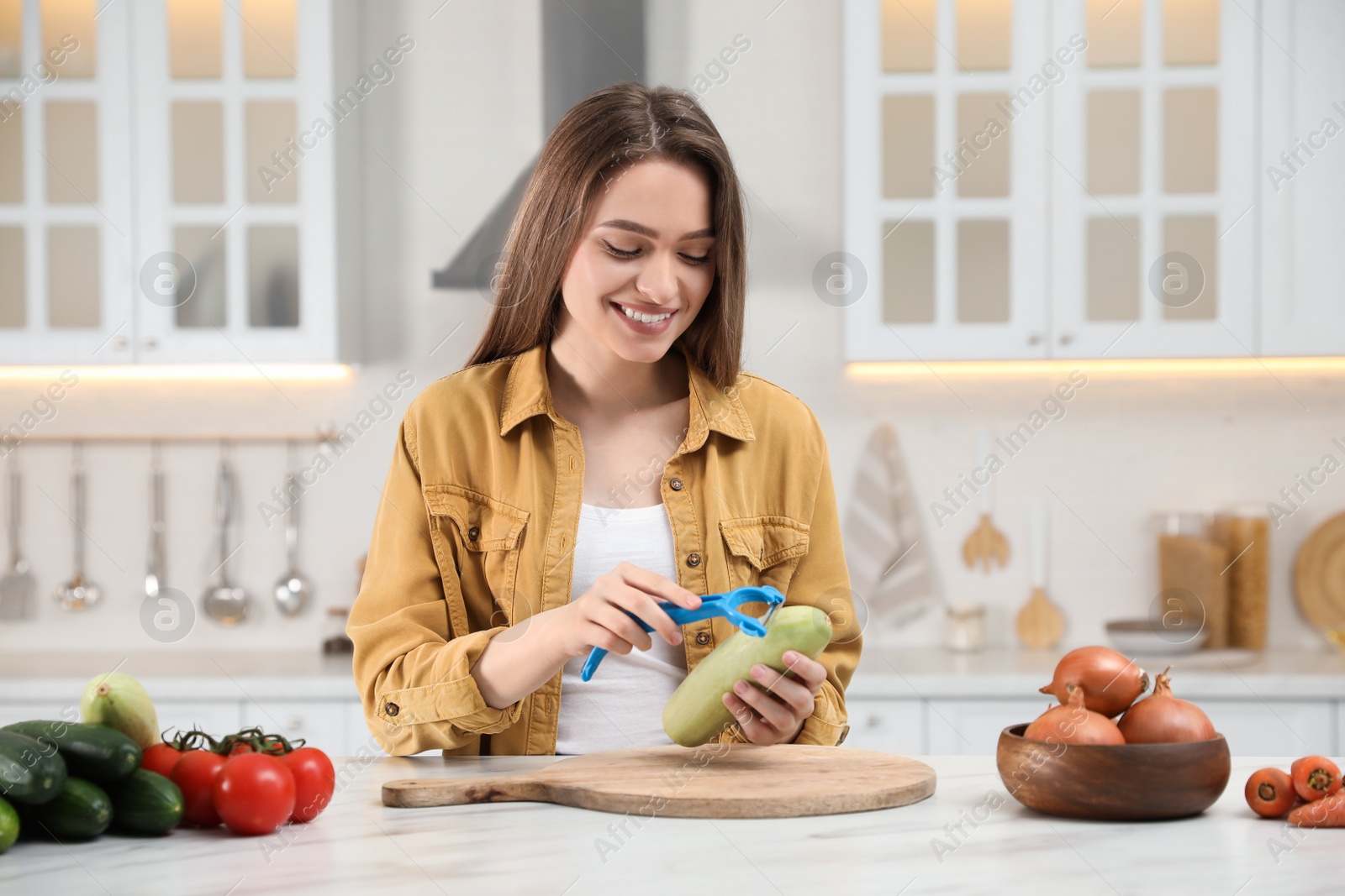 Photo of Young woman peeling zucchini at table in kitchen. Preparing vegetable