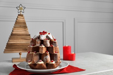 Photo of Delicious Pandoro Christmas tree cake with powdered sugar and berries near festive decor on white marble table. Space for text