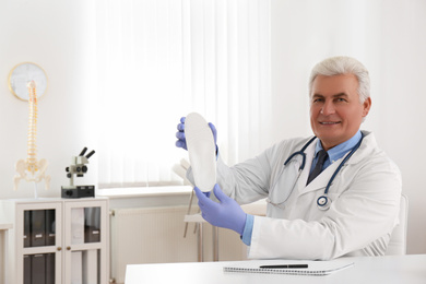 Photo of Senior male orthopedist showing insole in clinic