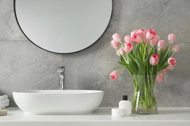 Photo of Vase with beautiful pink tulips near sink in bathroom