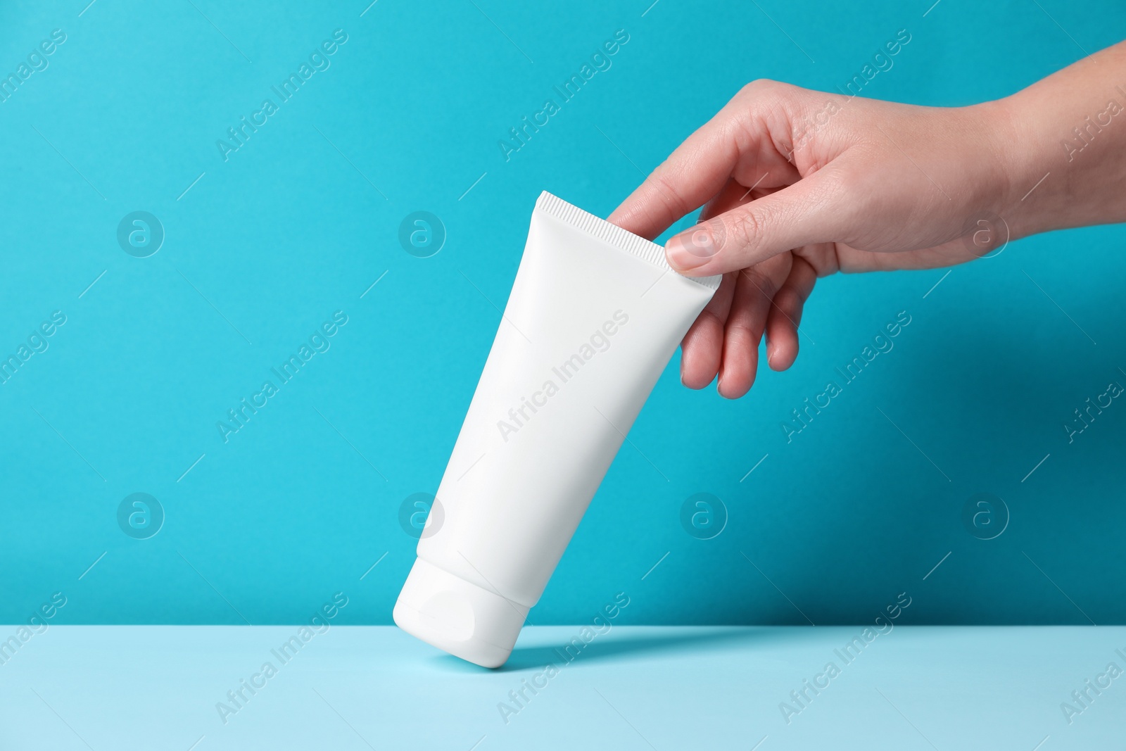 Photo of Woman with tube of hand cream at table against light blue background, closeup