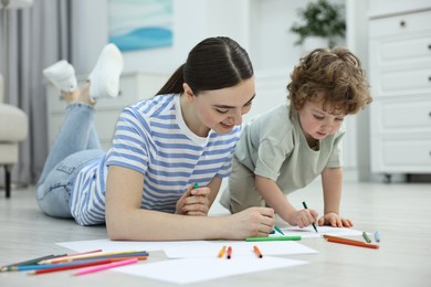 Photo of Mother and her little son drawing with colorful markers on floor at home