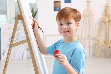 Photo of Little boy painting in studio. Using easel to hold canvas