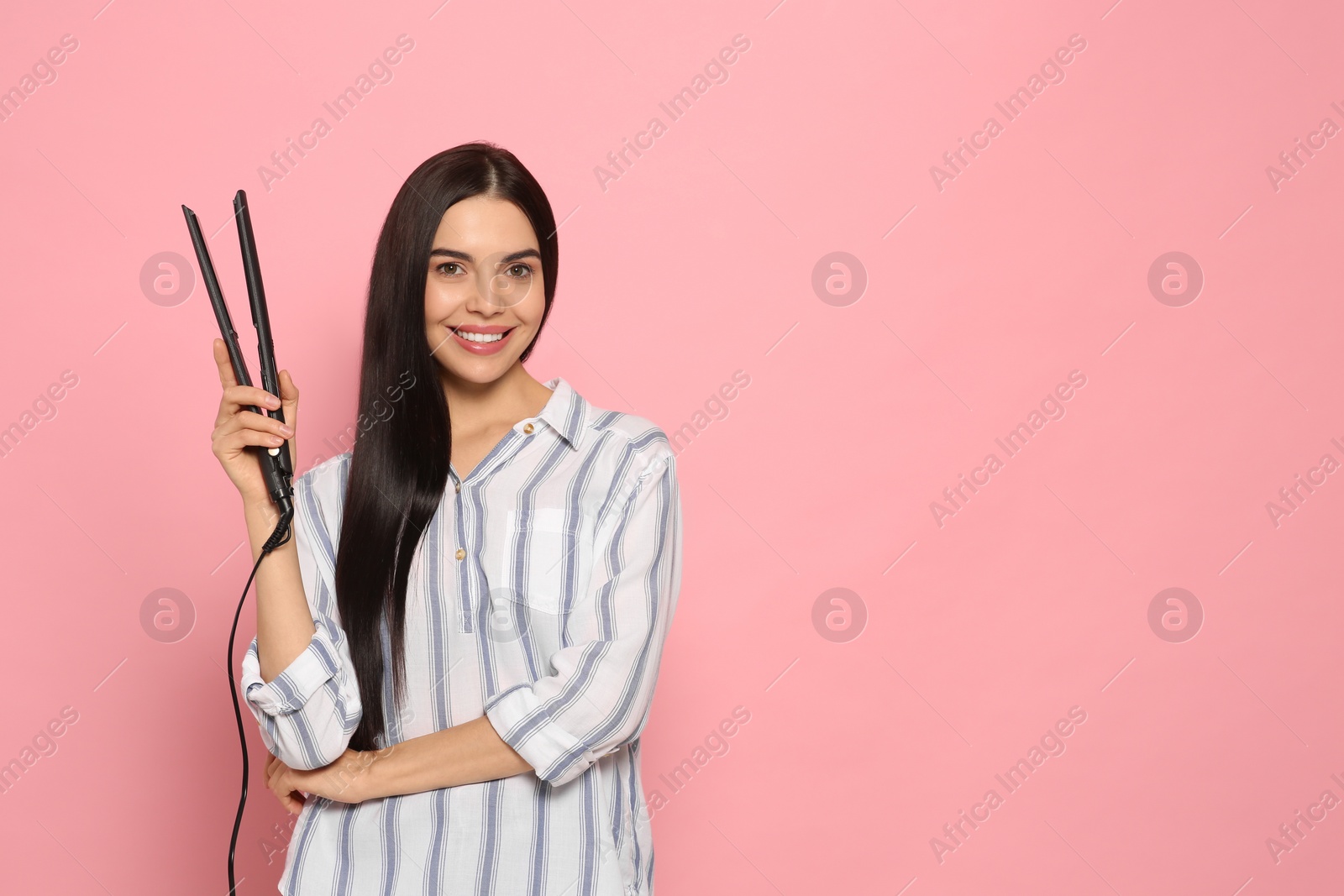 Photo of Beautiful happy woman with hair iron on pink background. Space for text