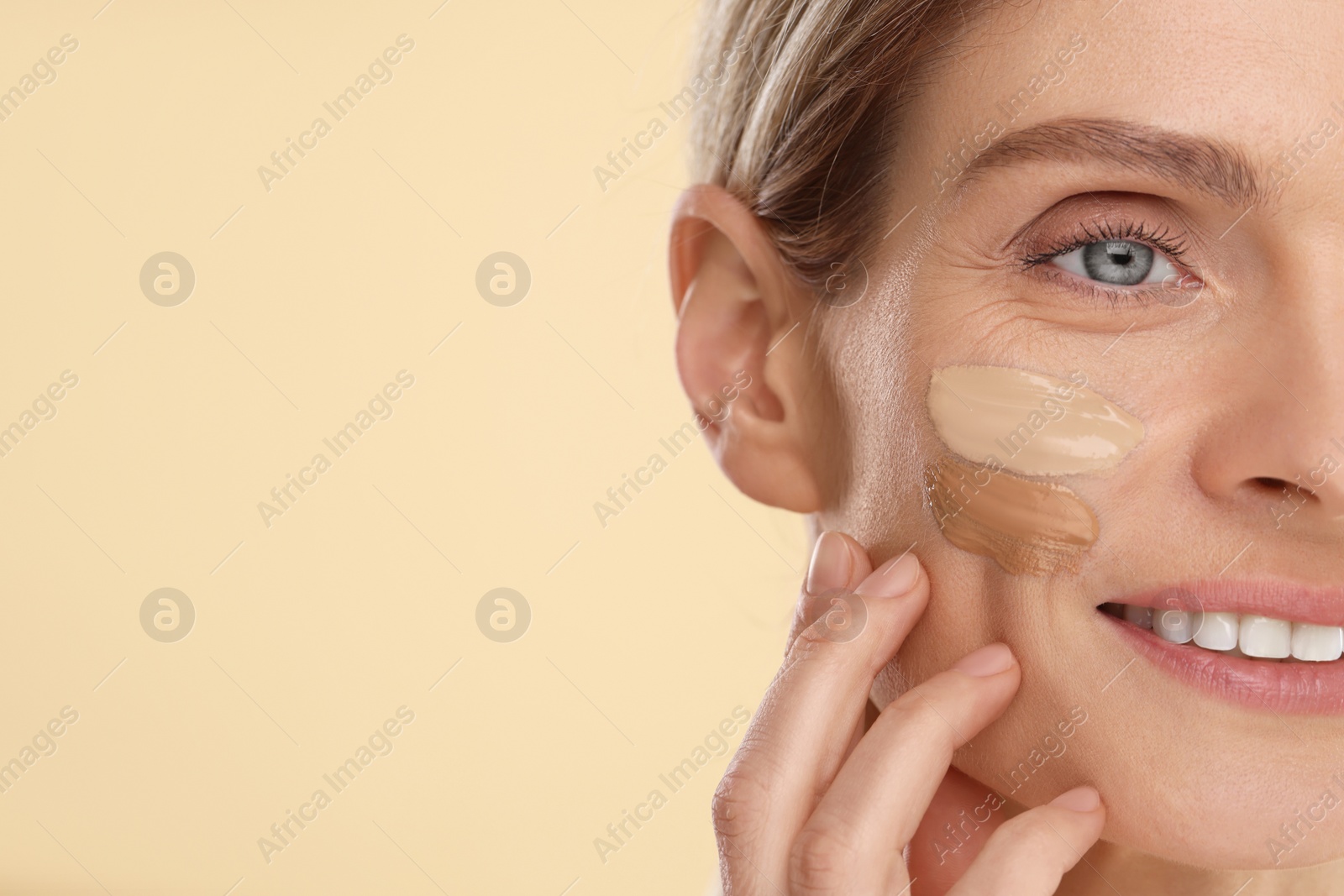 Photo of Woman with swatches of foundation on face against beige background, closeup. Space for text