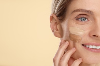 Photo of Woman with swatches of foundation on face against beige background, closeup. Space for text