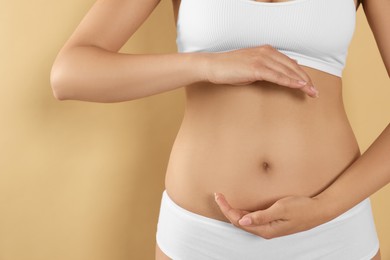 Photo of Woman in underwear holding something near her belly on beige background, closeup. Healthy stomach