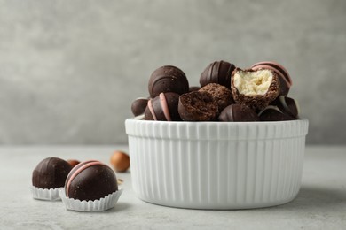 Different delicious chocolate truffles in bowl on light grey table