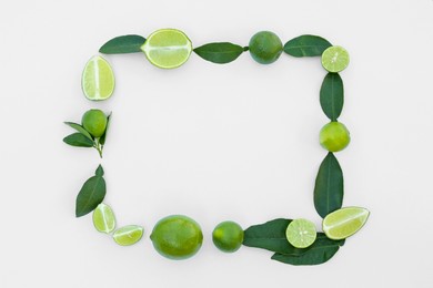 Photo of Frame made of fresh ripe limes and green leaves on white background, flat lay. Space for text