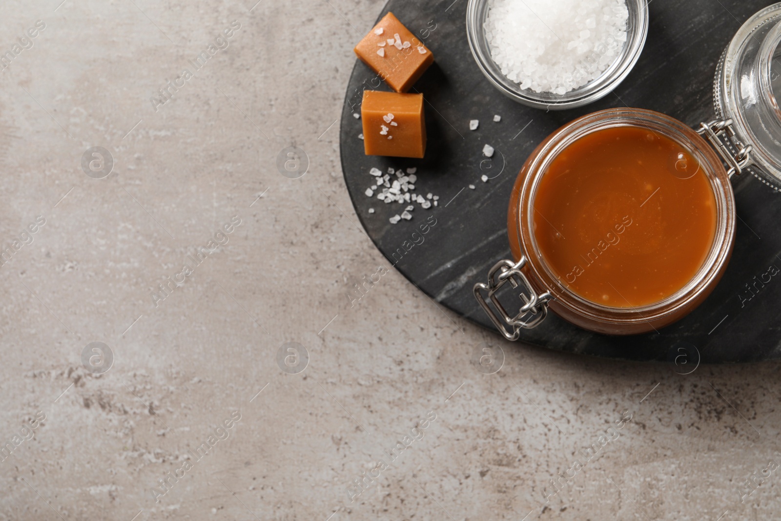 Photo of Tasty salted caramel in glass jar on grey table, flat lay. Space for text