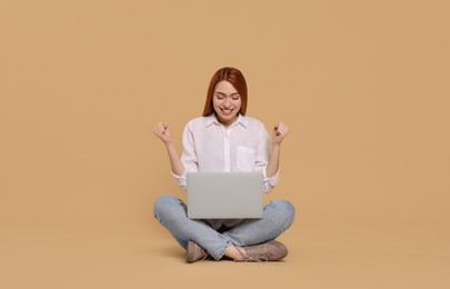 Happy young woman with laptop on beige background