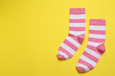 Photo of Striped pink and white socks on yellow background, flat lay. Space for text