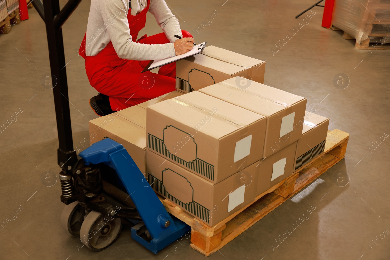 Image of Worker near manual forklift with cardboard boxes in warehouse, closeup. Logistics concept