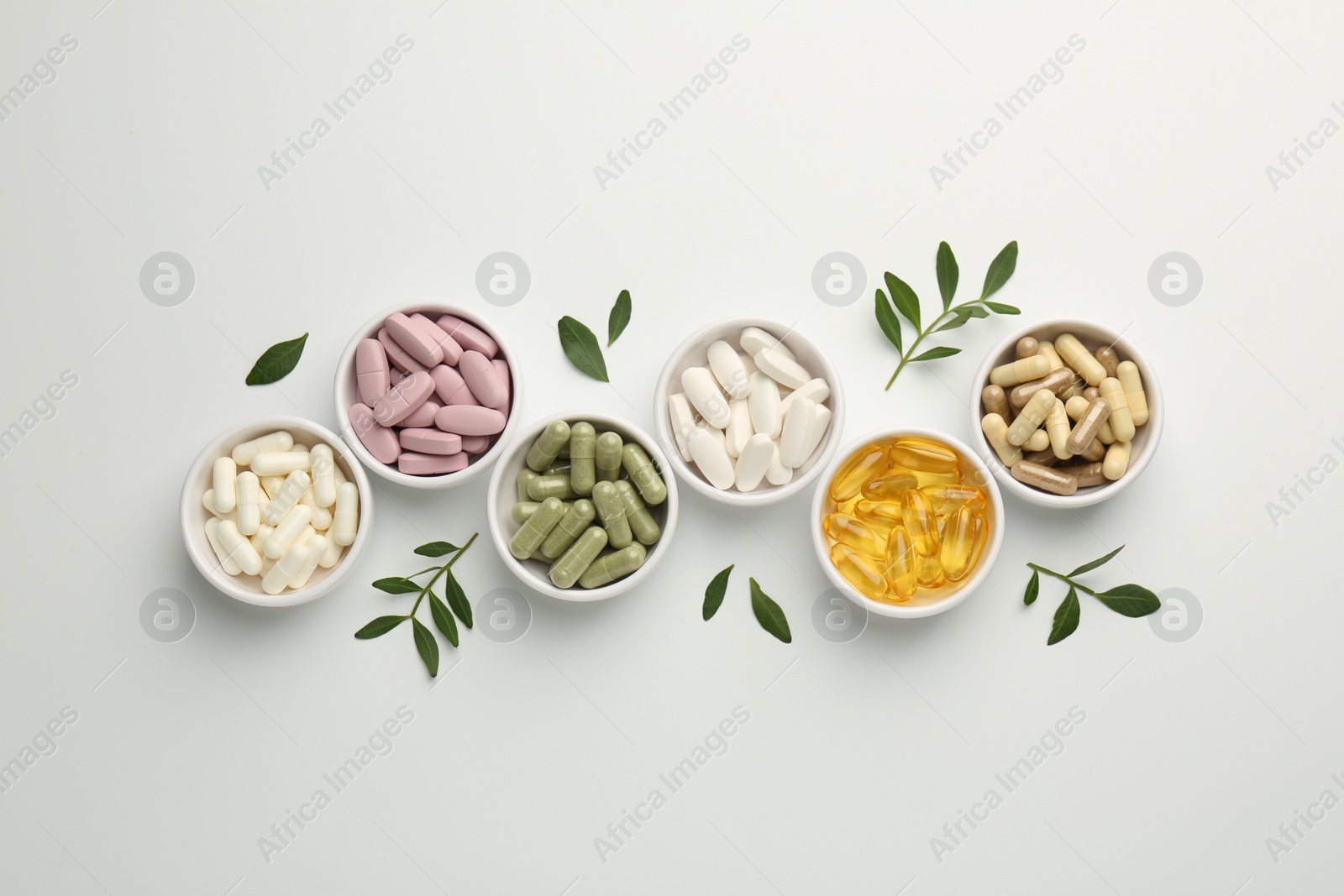 Photo of Different vitamin capsules in bowls and leaves on white background, flat lay