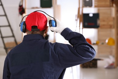 Photo of Worker wearing safety headphones indoors, back view. Hearing protection device