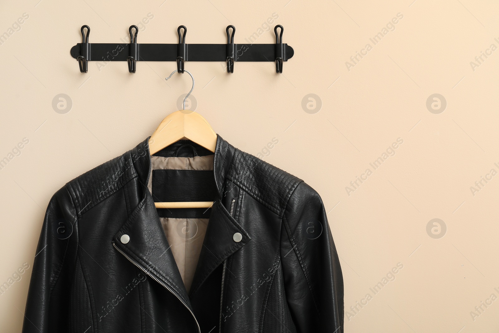 Photo of Hanger with black leather jacket on beige wall