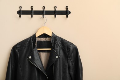 Hanger with black leather jacket on beige wall