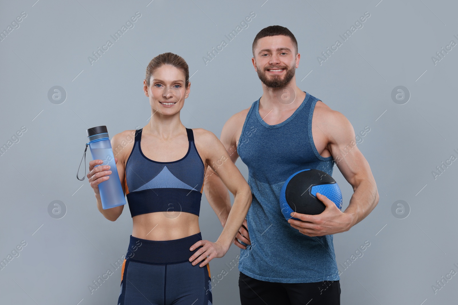 Photo of Athletic people with bottle of water and medicine ball on grey background