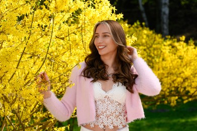 Beautiful young woman near blossoming shrub on spring day
