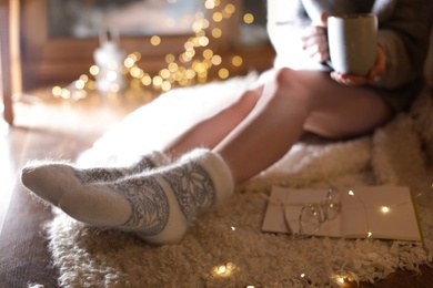 Woman with cup of hot beverage and book at home in winter evening, closeup