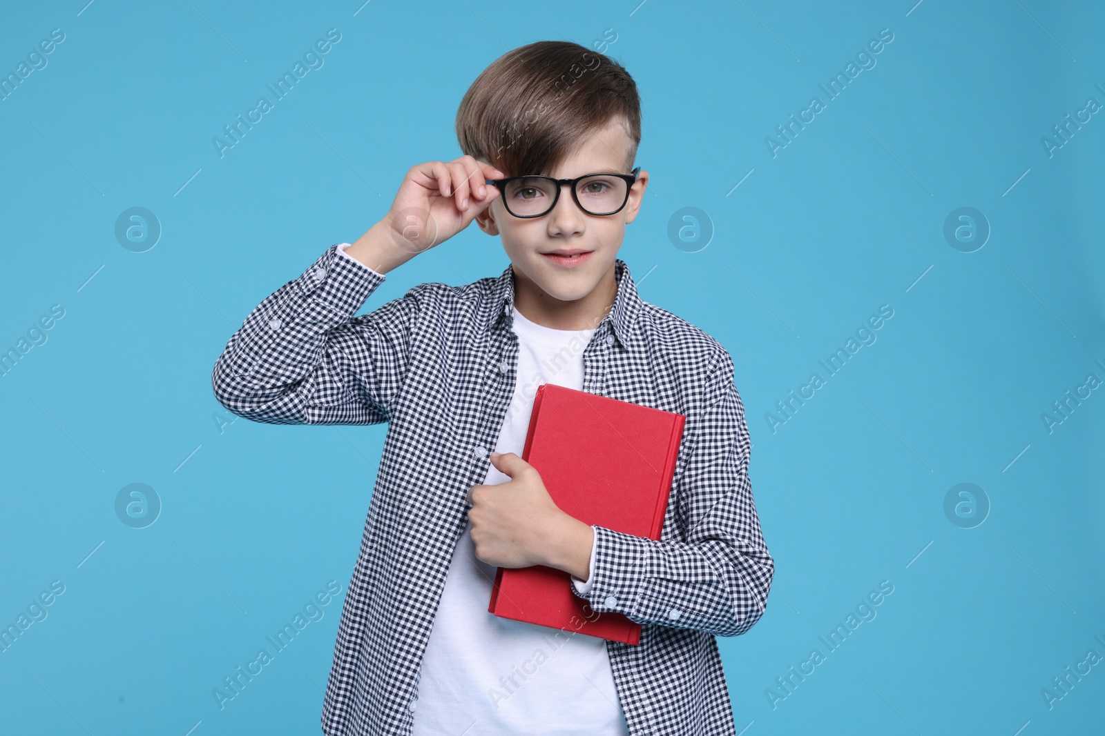 Photo of Cute schoolboy in glasses with book on light blue background