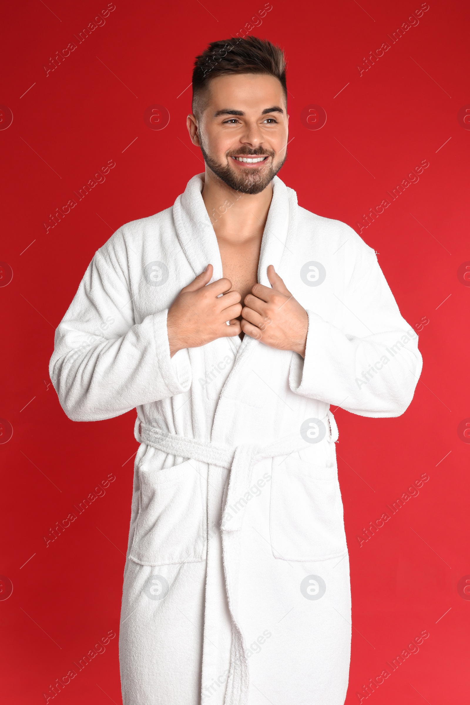 Photo of Happy young man in bathrobe on red background