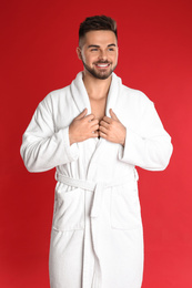 Photo of Happy young man in bathrobe on red background