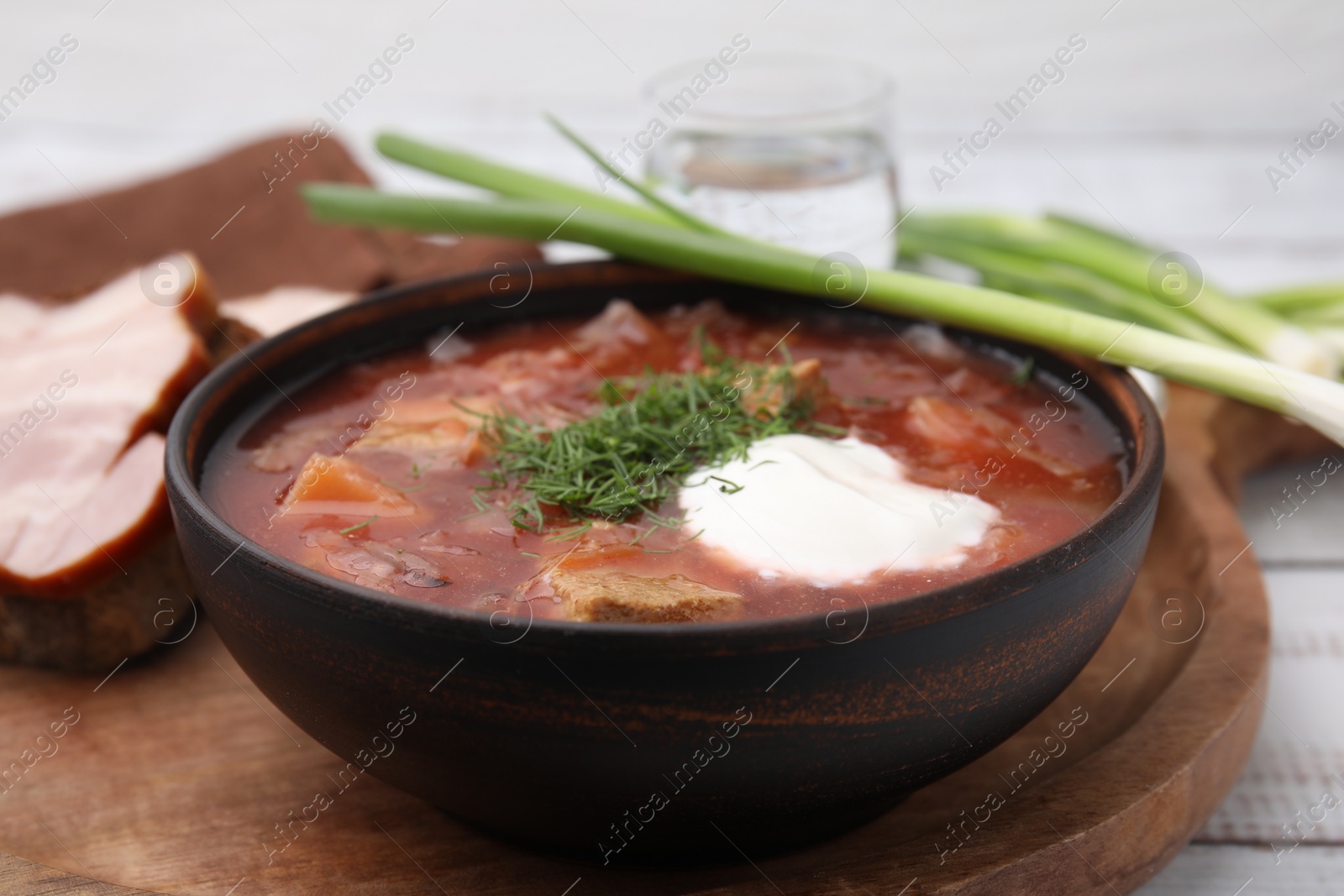 Photo of Tasty borscht with sour cream in bowl served with green onion on white wooden table, closeup