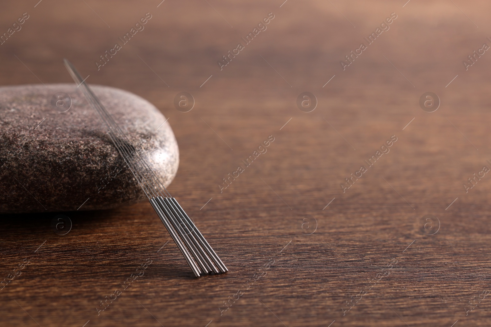 Photo of Acupuncture needles and spa stone on wooden table. Space for text