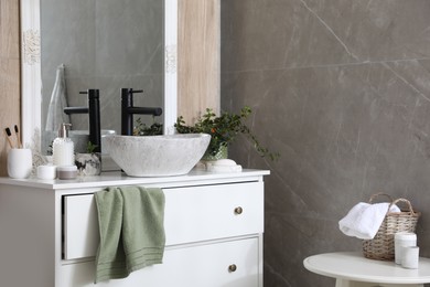 Chest of drawers with vessel sink, toiletries and houseplants in bathroom. Interior design