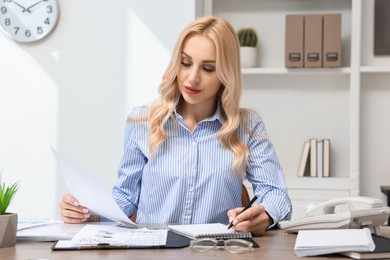 Secretary with document taking notes at table in office