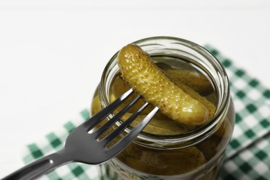 Photo of Fork with pickled cucumber over jar on white table, closeup