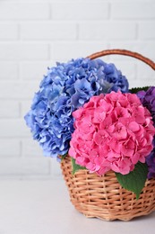 Photo of Bouquet with beautiful hortensia flowers in wicker basket on white wooden table near brick wall